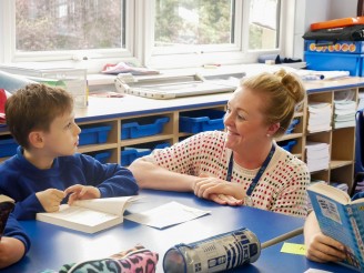 Teacher smiling at a student whilst they are reading