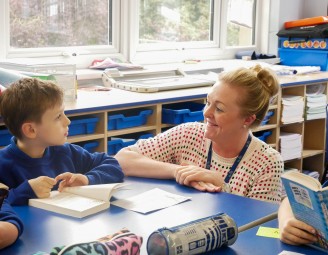 Teacher smiling at a student whilst they are reading