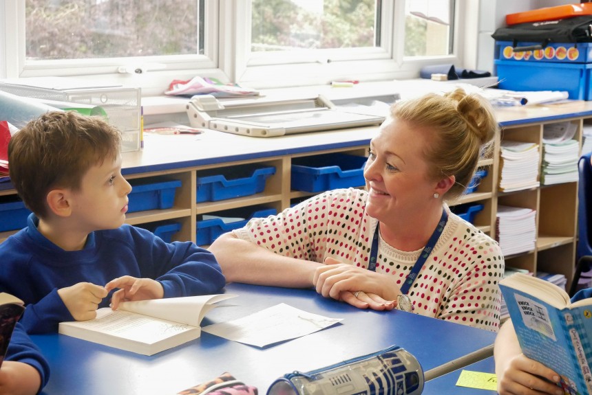 Teacher smiling at a student whilst they are reading