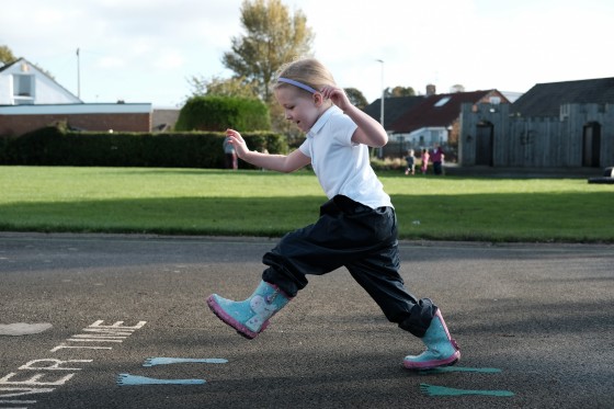 Child jumping in a playground wearing wellies and school uniform