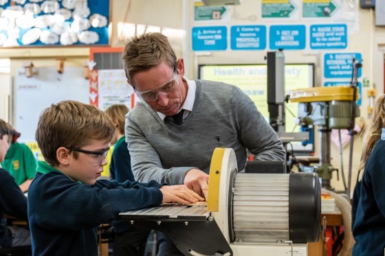 Teacher helping pupil on a woodwork machine